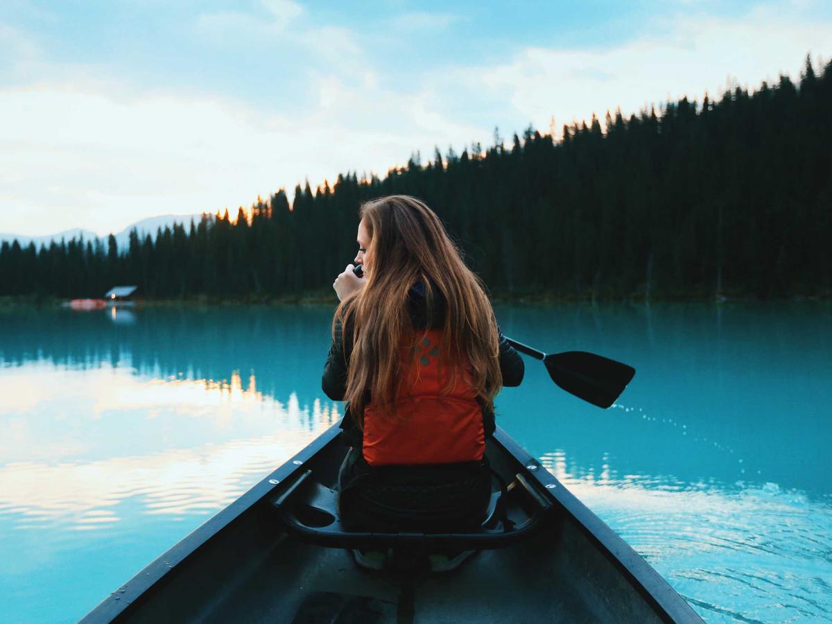 Seen over a paddler's shoulder from inside a canoe: still turquoise water and a dark tree line at dusk