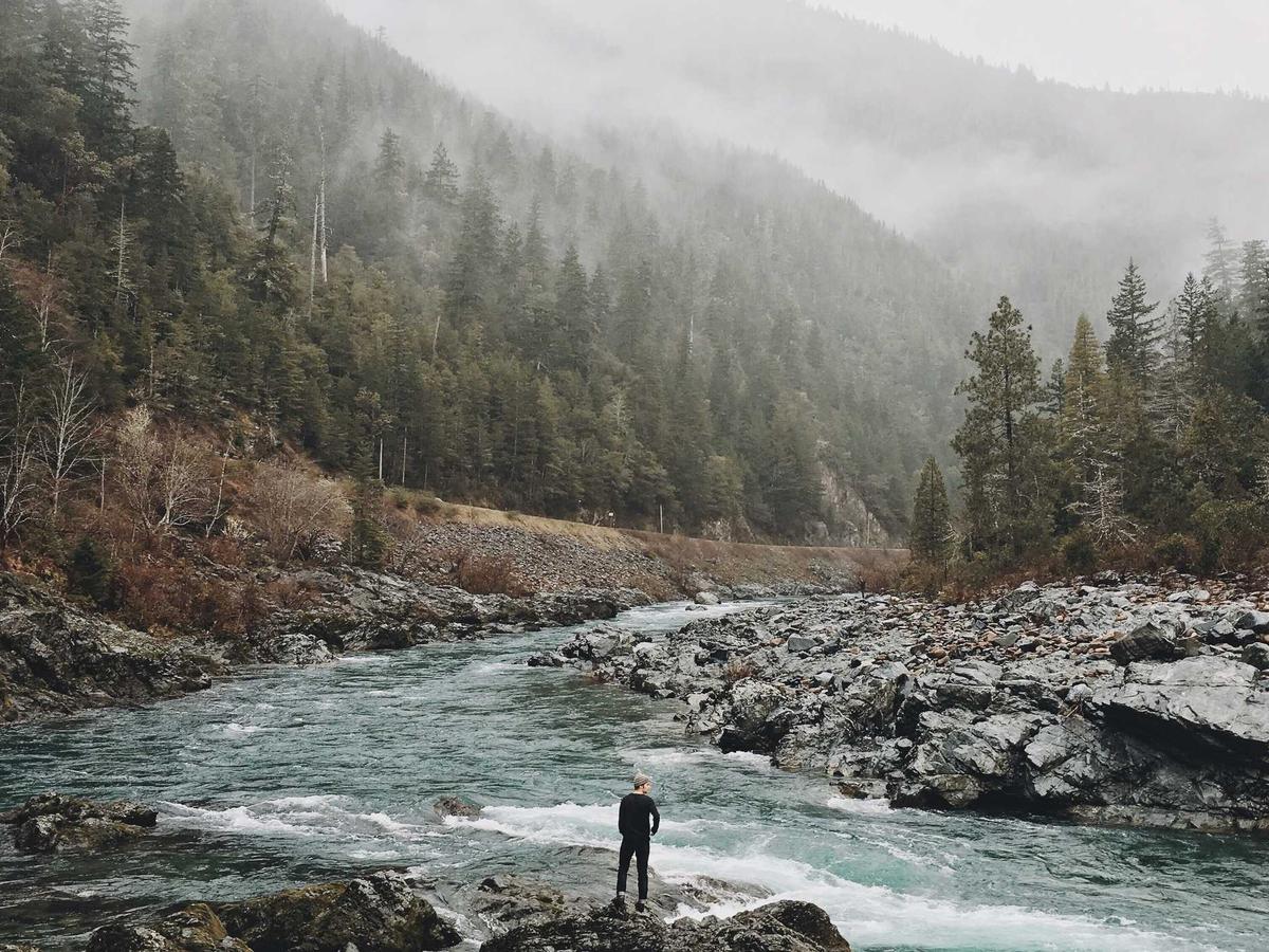 A lone figure standing by a river in morning fog